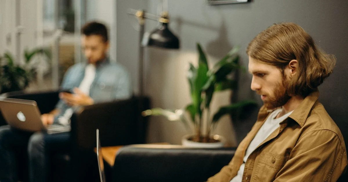 Deux hommes utilisant des ordinateurs portables dans un bureau moderne, mettant en avant les tendances du travail à distance.
