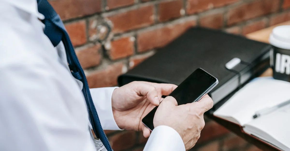 Un professionnel en tenue de travail utilisant un smartphone devant un mur en briques à l'intérieur.