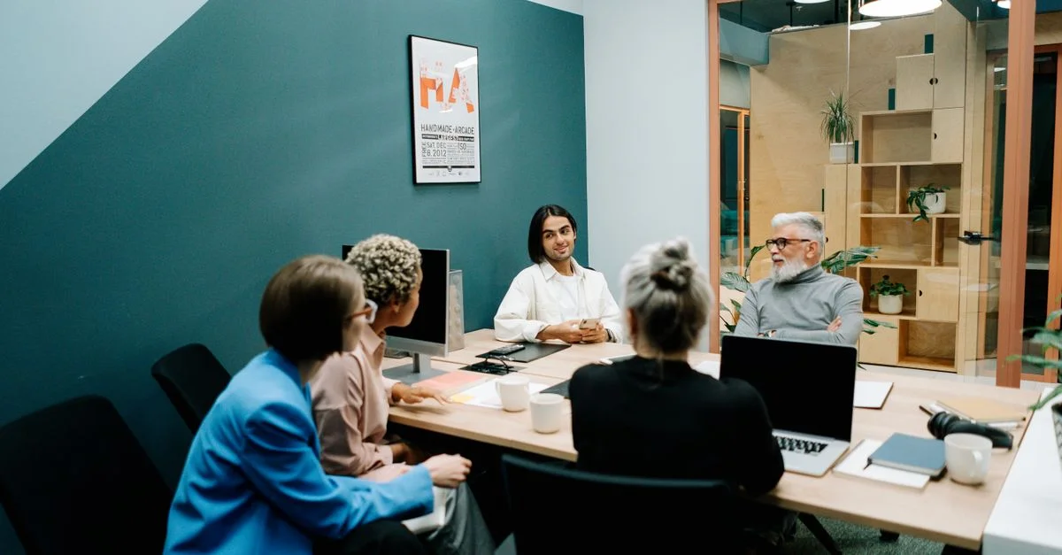 Groupe divers de professionnels ayant une réunion dans un espace de bureau moderne, discutant de projets avec des ordinateurs portables et des notes.