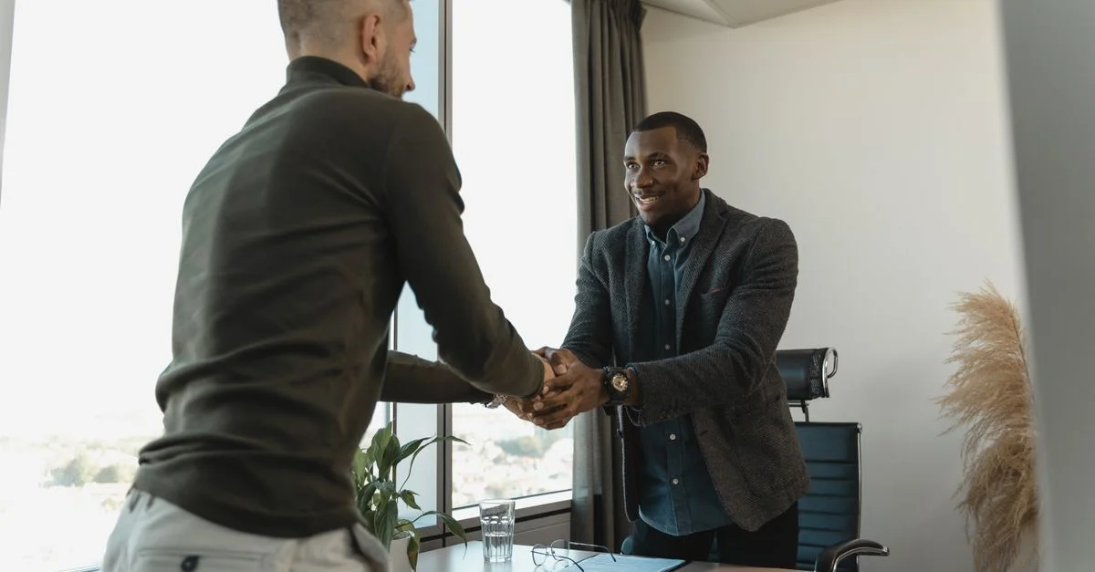 Deux hommes d'affaires échangeant une poignée de main lors d'une réunion professionnelle dans un bureau moderne.