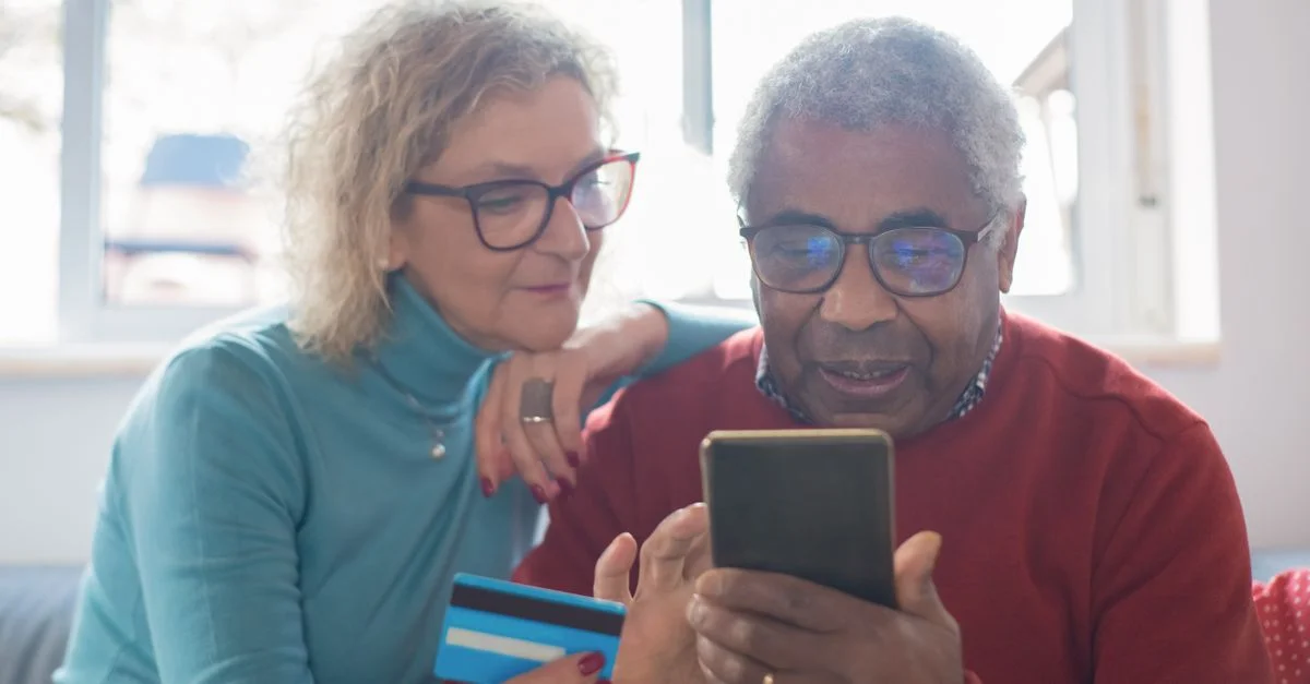 Couple senior utilisant un smartphone pour faire des achats en ligne avec une carte de crédit à l'intérieur.