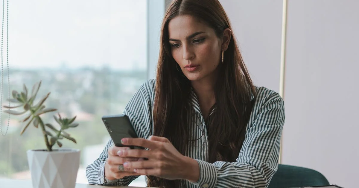 Une femme d'affaires utilisant attentivement son smartphone à un bureau dans un cadre de bureau moderne avec une plante en pot.
