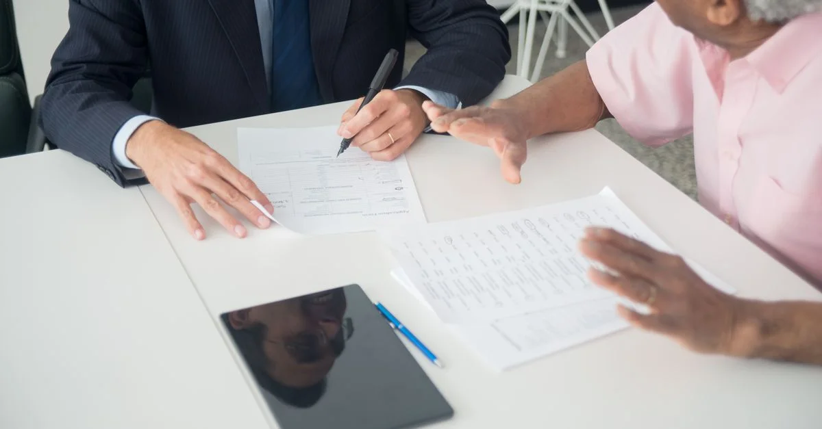 Une réunion d'affaires entre un client âgé et un consultant discutant de documents à une table de bureau.